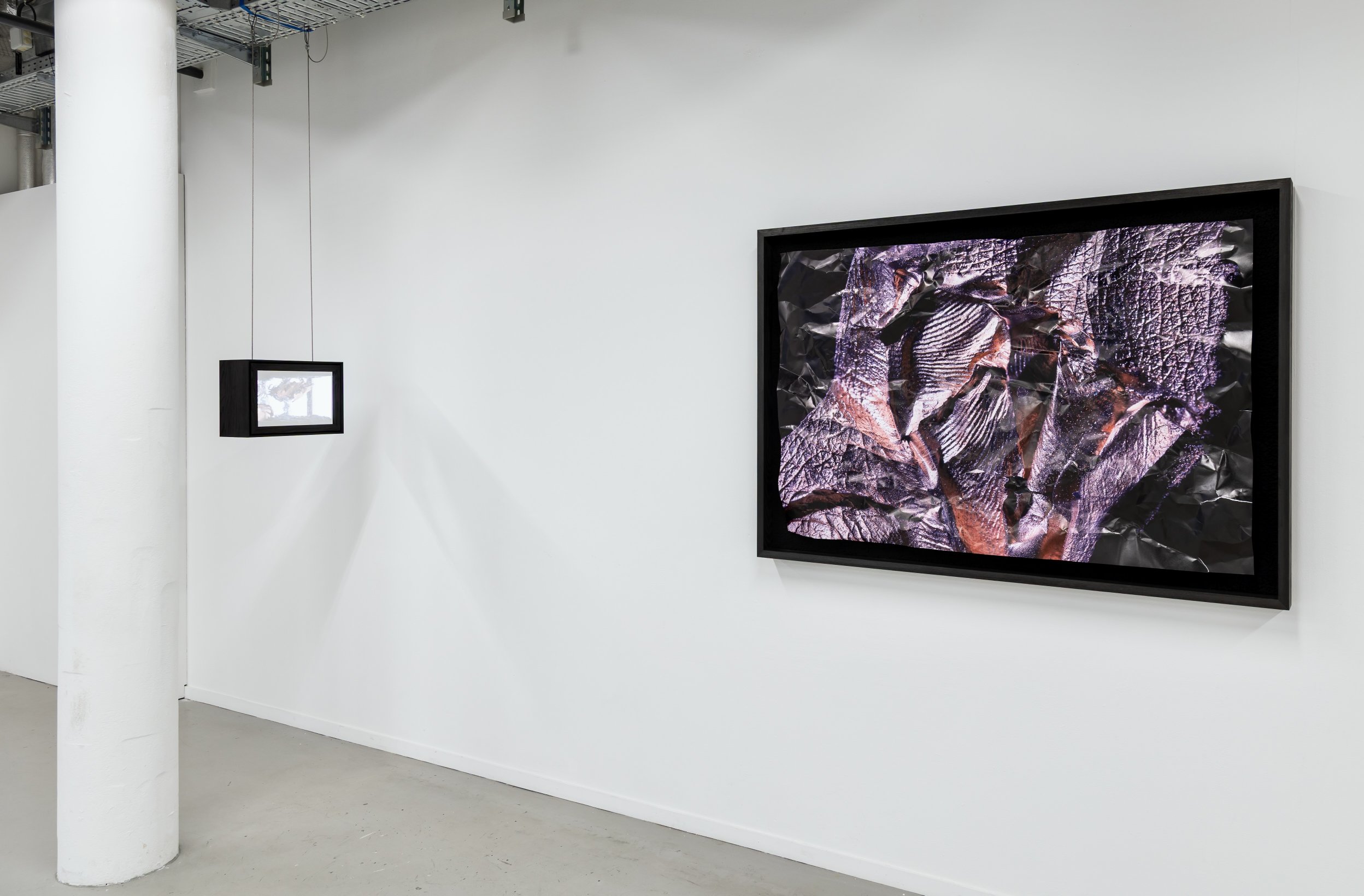 Gallery view of a small illuminated light-box sculpture beside a large framed textured photographic print