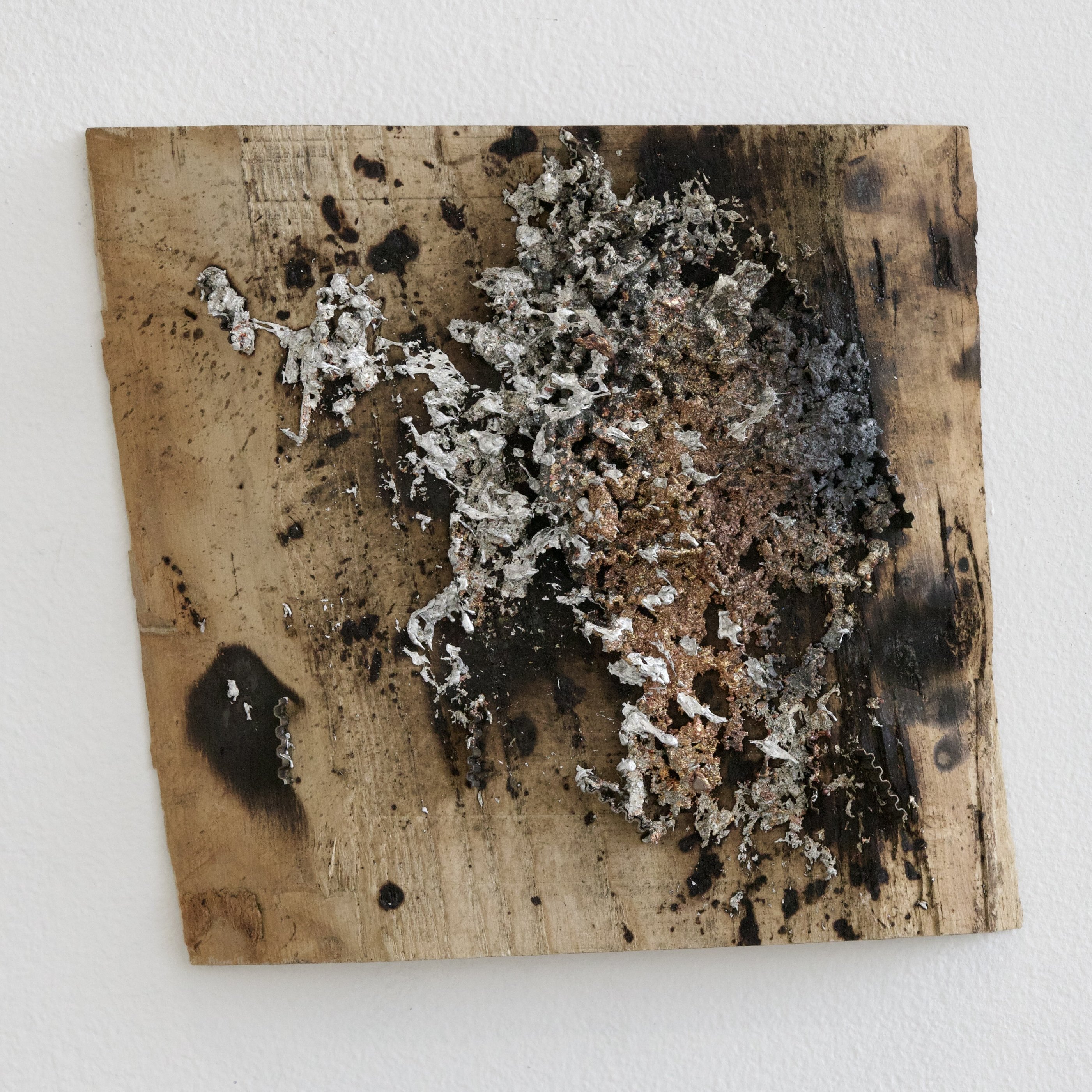 Square charred wood panel with a dense cluster of sprayed aluminium, steel and copper metal deposits