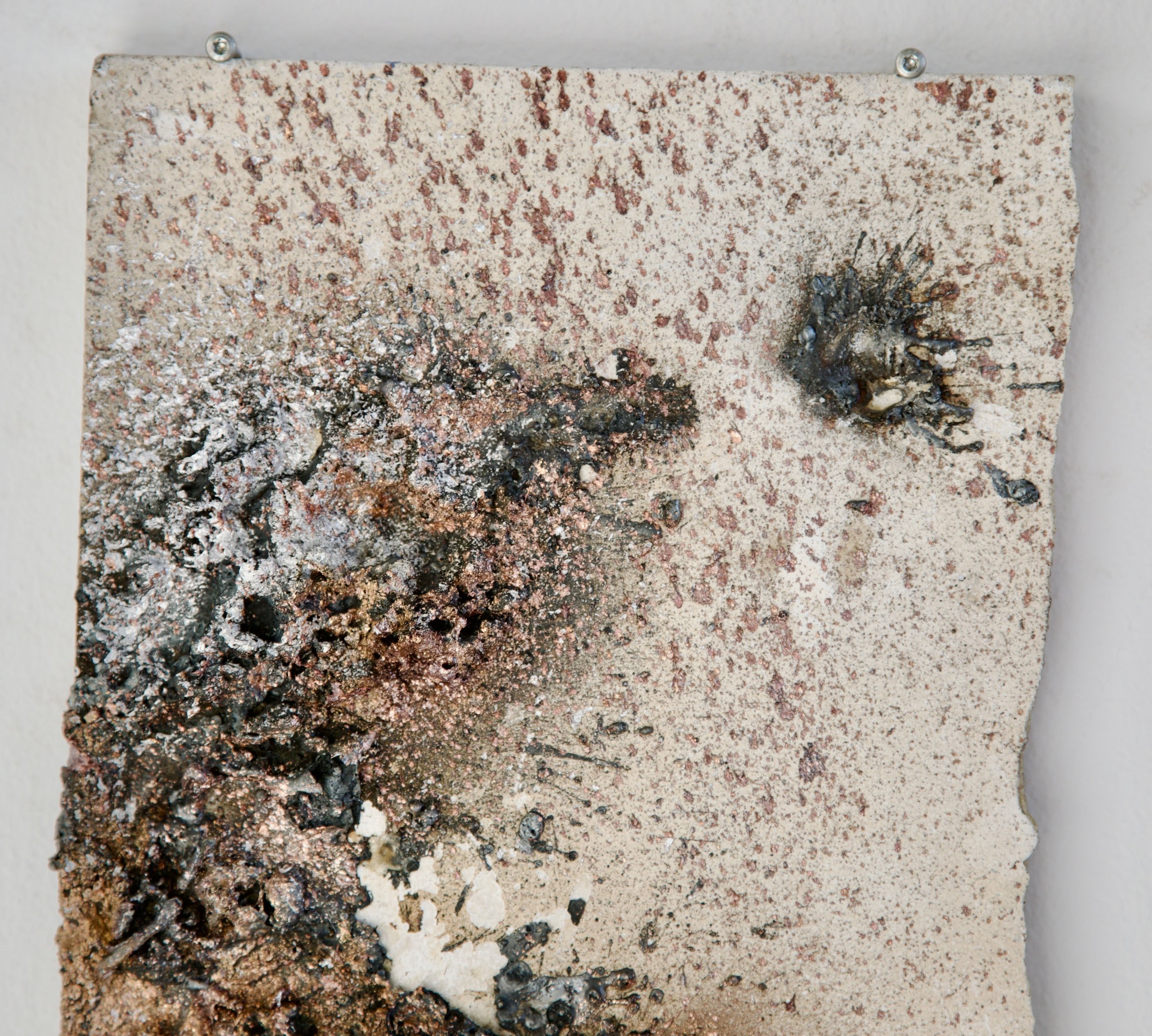 Detail of sprayed metal deposit on speckled mineral tile