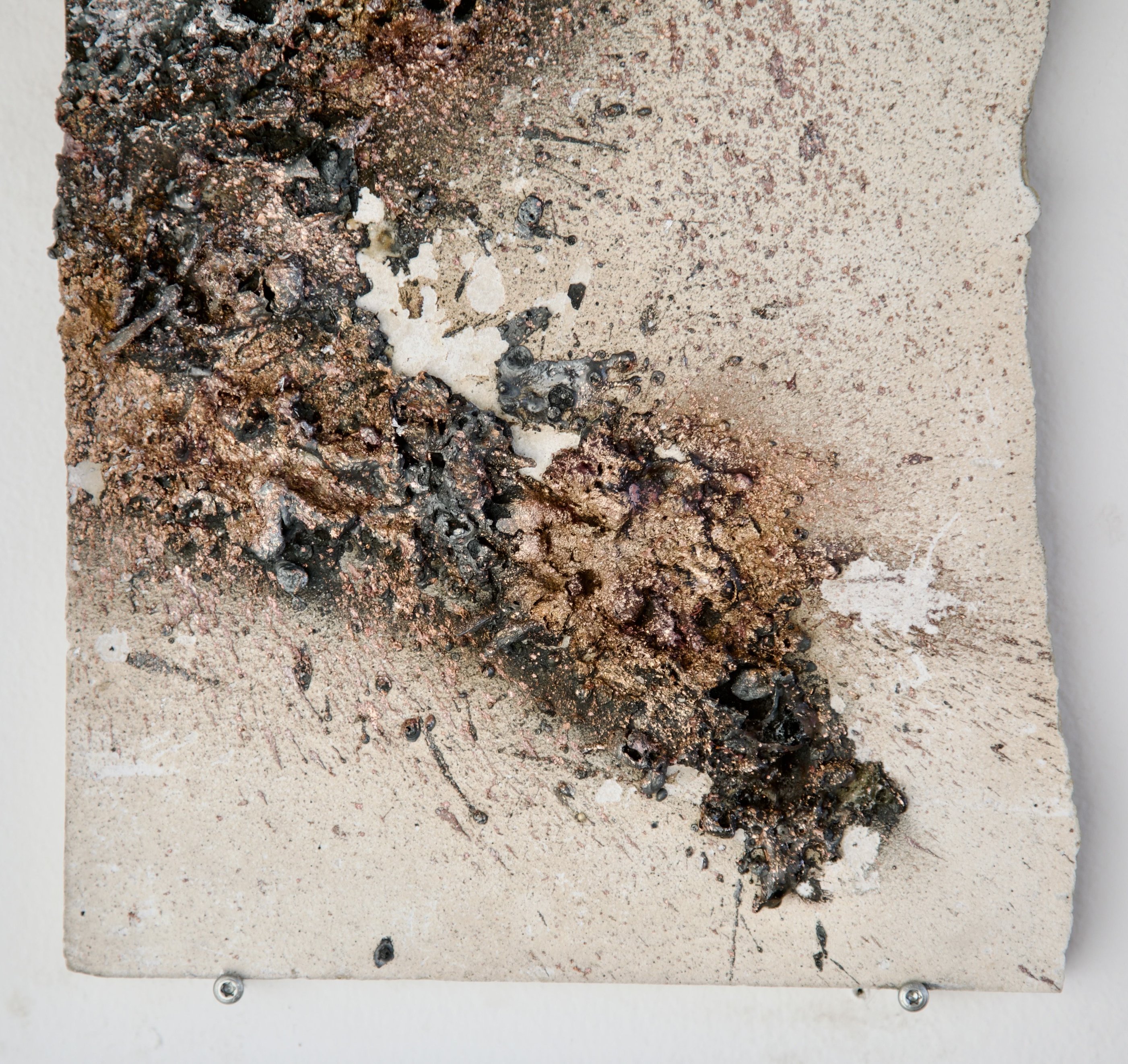 Detail of sprayed metal deposit on speckled mineral tile